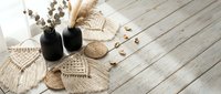 Cozy home decor flat lay with macrame crafts, dried eucalyptus in black vases, and natural textures on rustic white wooden background for interior design.