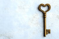 Vintage golden key with heart-shaped handle on white textured background. Antique brass metal object isolated for romantic design concepts and love themes.