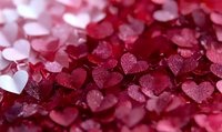 Pink and red heart-shaped confetti with glitter texture creates romantic background pattern. Macro shot shows delicate sparkle detail for Valentine's Day and love themes.