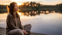 Young woman meditating peacefully on wooden dock at sunset by calm lake, enjoying serene moment in nature during golden hour for mindfulness and relaxation.