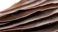 Smooth waves of dark chocolate with tiny air bubbles creating texture and depth, macro photography showing rich brown tones and glossy surface detail.