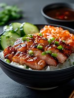 Grilled teriyaki chicken slices on white rice with fresh cucumber, salmon sashimi and green onions in black bowl, served with soy sauce on dark background.