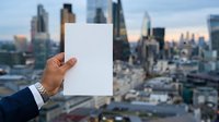 Businessman holding blank white card with urban skyline in background, corporate presentation mockup.
