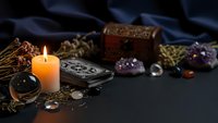Mystical fortune telling setup with burning candle, tarot cards, crystals and ornate jewelry box on dark surface for spiritual guidance and divination.