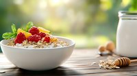 Healthy breakfast bowl with oatmeal, fresh raspberries, honey and mint leaves on wooden table with morning sunlight and milk jar in background.