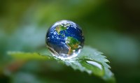 Planet Earth reflected in water drop on green leaf surface with natural bokeh background showing environmental conservation and nature concept.