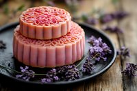 Traditional pink mooncakes with intricate floral patterns on dark plate with lavender flowers for Mid-Autumn Festival celebration and cultural cuisine.