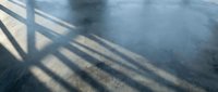 Dramatic shadows cast by railing or fence create striking geometric patterns on wet pavement surface after rain, perfect for urban design projects.