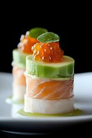 Elegant sushi appetizer with fresh salmon, cucumber, red caviar and mint leaf garnish on white plate against dark background, macro food photography.