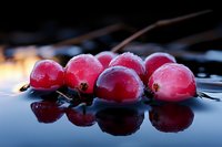 Fresh red currants with water drops on dark reflective surface in dramatic lighting, macro photography showing vibrant berries with natural morning dew.