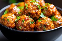 Glazed meatballs garnished with fresh herbs in black bowl, close up view. Juicy appetizer coated in sweet and savory Asian-style sauce, served as party food.