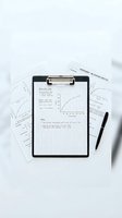 Clipboard with mathematical equations, graphs, and calculations on grid paper surrounded by scientific documents and black pen on white surface for education and research.