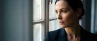 Professional businesswoman gazing thoughtfully through office window, contemplating future decisions in corporate environment with natural lighting.