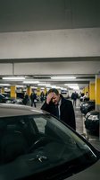 Stressed businessman holding head in hands next to car in underground parking garage expressing frustration and overwhelm.