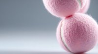 Pink tennis balls stacked on clean white surface with soft lighting for sports equipment photography and athletic gear marketing materials.