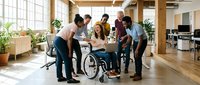 Diverse business team collaborating with female colleague in wheelchair during office meeting. Inclusive workplace teamwork and accessibility concept.