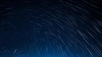 Long exposure star trails create concentric circles in dark night sky, with silhouetted mountain peaks visible along bottom horizon against starry background.