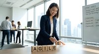 Professional Asian businesswoman arranging wooden letter blocks spelling AGILE in modern office conference room with team meeting in background.