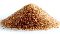 Heap of raw brown sugar crystals on white background, natural sweetener ingredient for baking and cooking.