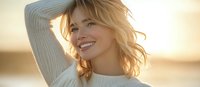 Young blonde woman in white sweater smiling with natural sunlight creating warm backlight, expressing joy and carefree attitude during golden hour.
