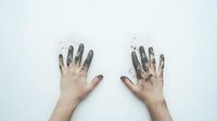Dirty hands with black paint or charcoal against white background showing creative artistic process and messy workspace atmosphere. Flat lay composition.