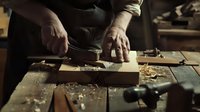 Craftsman hands working with wood planer on rustic workbench, wood shavings scattered around traditional carpentry tools in warm workshop lighting.