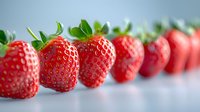 Fresh ripe strawberries in row on light blue background, selective focus on first berry. Natural organic fruit macro photography for healthy eating concept.