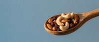 Mixed nuts and dried fruits in wooden spoon on blue background for healthy snacking and cooking ingredients.