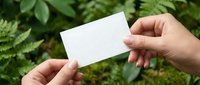 Hand holding blank white business card mockup against natural green foliage background for branding and corporate identity design projects.