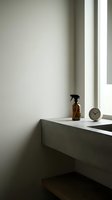 Minimalist workspace with amber spray bottle and round clock on concrete desk near bright window, conveying clean, modern interior design aesthetic.