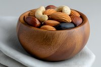 Mixed nuts and dried fruits in wooden bowl on white cloth background for healthy snacking and cooking ingredients.