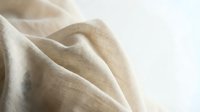 Soft beige linen fabric with natural texture and gentle folds creating elegant drapery for interior design and textile applications.