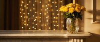 Yellow roses in glass vase on wooden table with warm bokeh lights creating cozy home interior atmosphere for romantic occasions and celebrations.