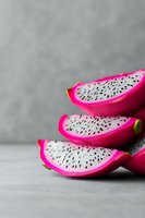 Fresh dragon fruit slices with vibrant pink skin and white flesh with black seeds arranged in minimalist composition against gray background.