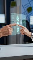 Two business professionals interact with a holographic touchscreen displaying growth charts, data analytics, and workflow diagrams in a modern office environment for technology and innovation concepts.