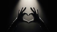 Silhouette of hands forming heart shape against dramatic spotlight background. Romantic gesture symbolizing love, affection and emotional connection in black and white.