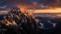 Dramatic mountain peak bathed in golden sunrise light with orange and purple clouds creating stunning alpine landscape scenery for outdoor adventure content.
