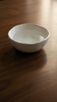 Empty white ceramic bowl on wooden table with warm natural light casting soft shadows, suitable for food styling and tableware design projects.