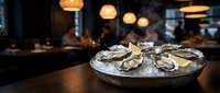 Fresh oysters on ice platter with lemon garnish served in upscale restaurant with warm ambient lighting and blurred dining room background.