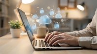 Professional working on laptop with cloud computing security icons floating above keyboard in modern office environment for digital transformation.