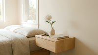 Minimalist wooden floating nightstand with drawer beside bed in bright modern bedroom interior with white flower vase and natural lighting.