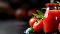 Fresh tomato juice in glass bottle with raw ripe tomatoes and green leaves on dark background. Natural healthy beverage concept for detox drinks.