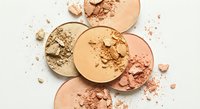 Crushed makeup powder compacts in neutral beige and pink tones scattered on white background for cosmetic beauty product photography and design projects.