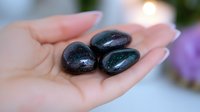 Polished black obsidian healing stones resting in open palm against soft blurred background, showcasing natural mineral texture and metaphysical properties.