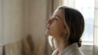 Young woman with brown hair looking up thoughtfully in bright indoor setting with natural window light creating peaceful contemplative mood for wellness content.