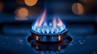 Blue gas flame burning on kitchen stove burner with bokeh lights in dark background, close up macro shot showing energy consumption and cooking concept.
