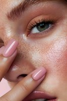 Close-up of young woman's face with natural freckles, dewy glowing skin, pink manicured nails, and green eyes showcasing fresh minimal makeup look for beauty and skincare.