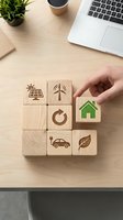 Hand placing wooden blocks with eco-friendly symbols on office desk representing sustainable business practices and green energy solutions.
