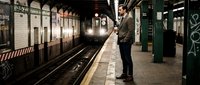 Young businessman in suit waiting for subway train at underground station platform during evening commute in urban metro system.