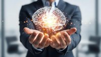 Professional businessman in dark suit holding glowing digital brain hologram with light effects representing artificial intelligence and innovation concepts.